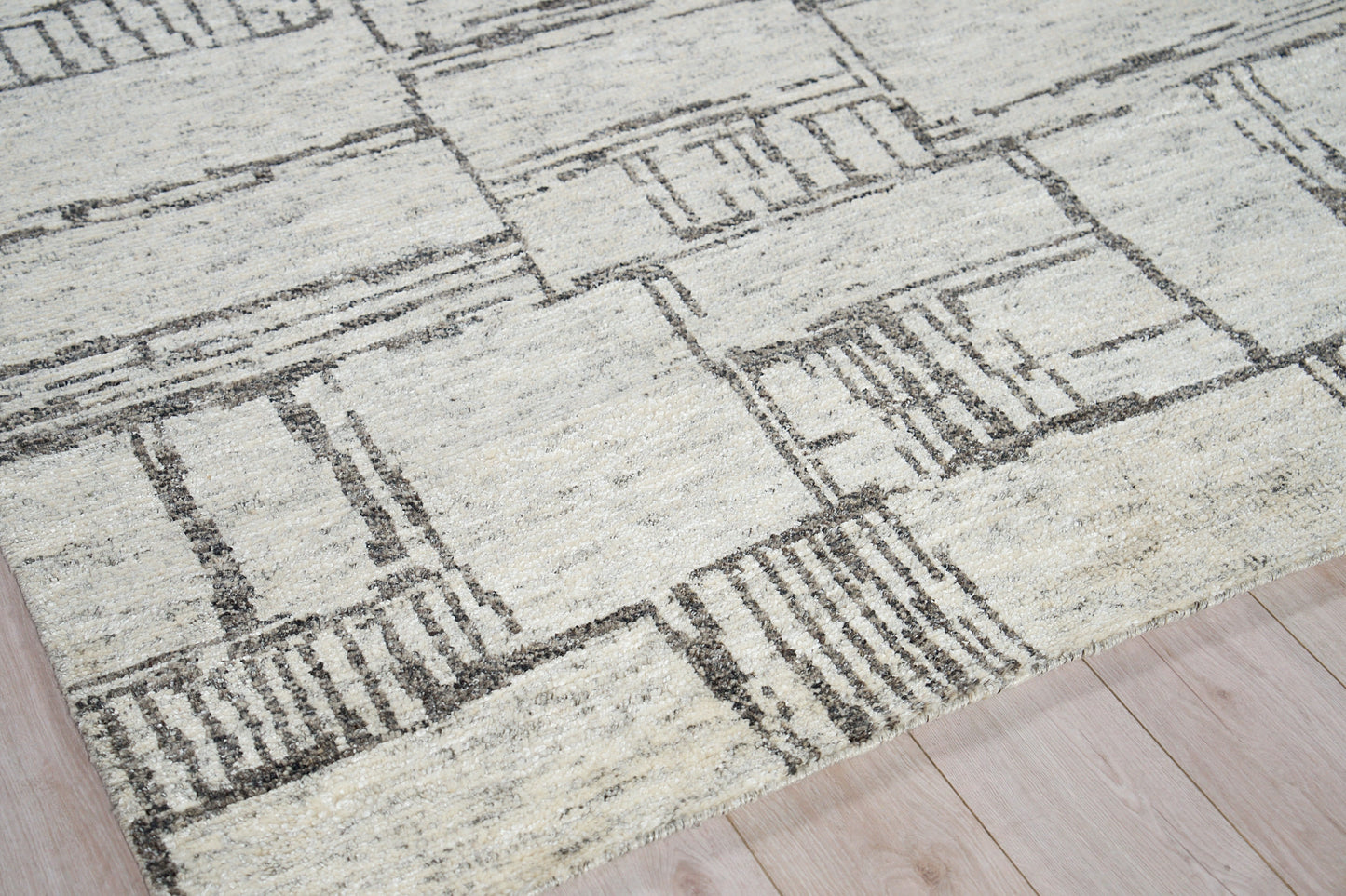 Cream and gray geometric area rug with rectangular blocks and hand-knotted pile on a light wood floor.
