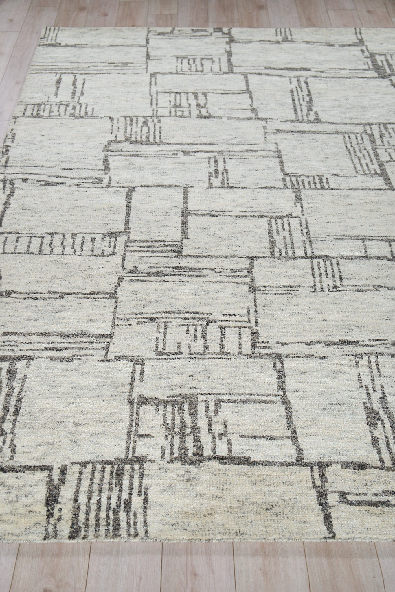 Light beige geometric area rug with dark gray rectangular blocks; modern low-pile, abstract patchwork design.