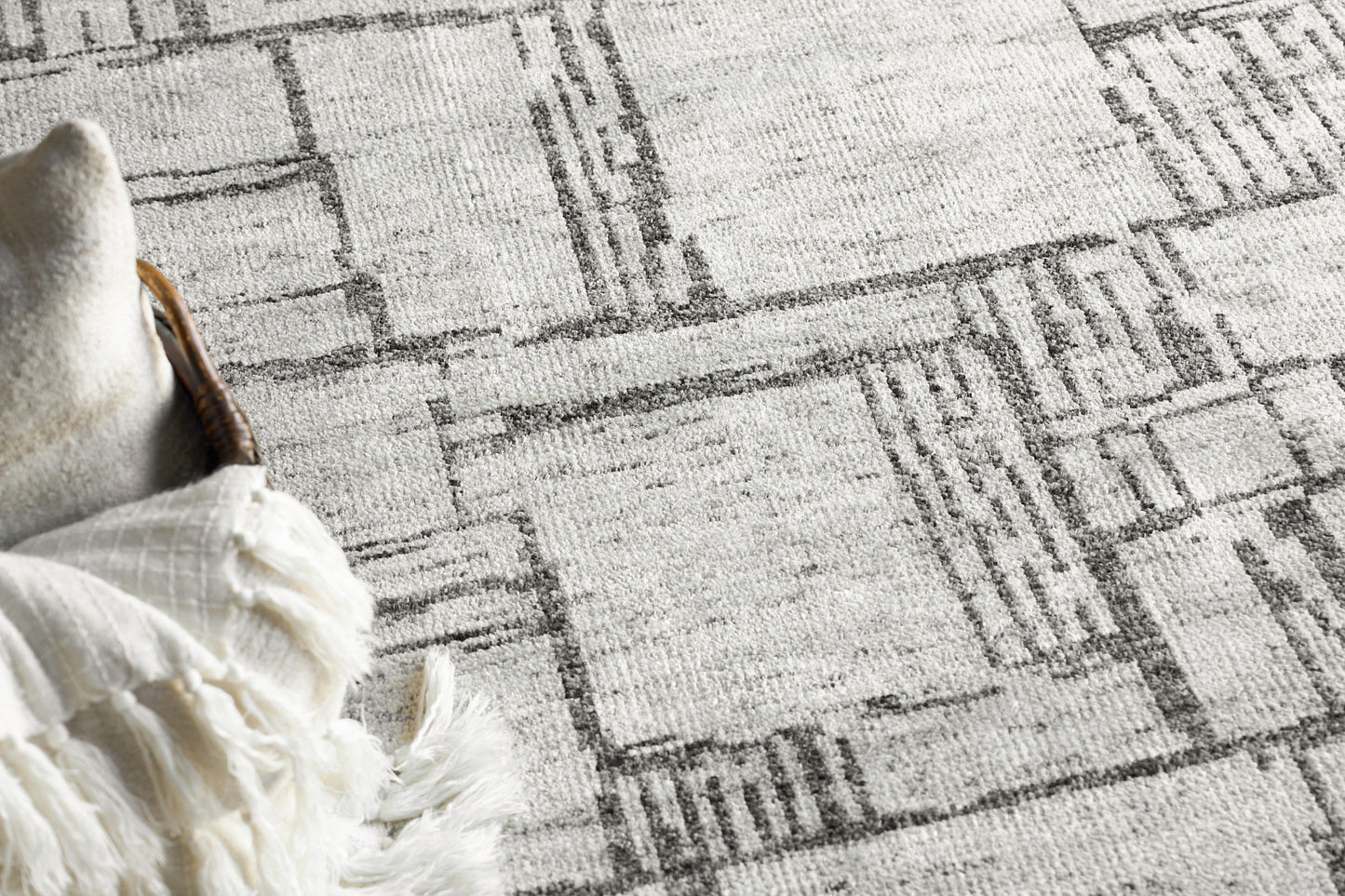 Gray geometric area rug with a distressed rectangular pattern; white fringed edge along the left side.