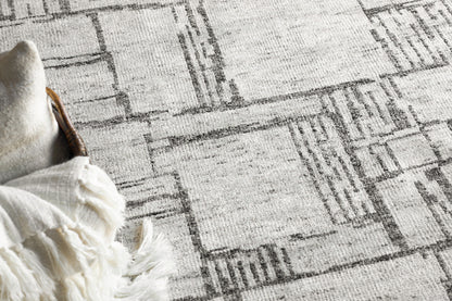 Gray geometric area rug with a distressed rectangular pattern; white fringed edge along the left side.