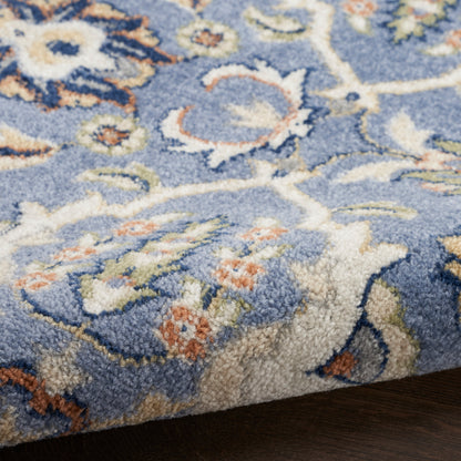 Blue floral-patterned plush rug with cream, peach and olive accents, Persian-inspired design on dark hardwood floor.