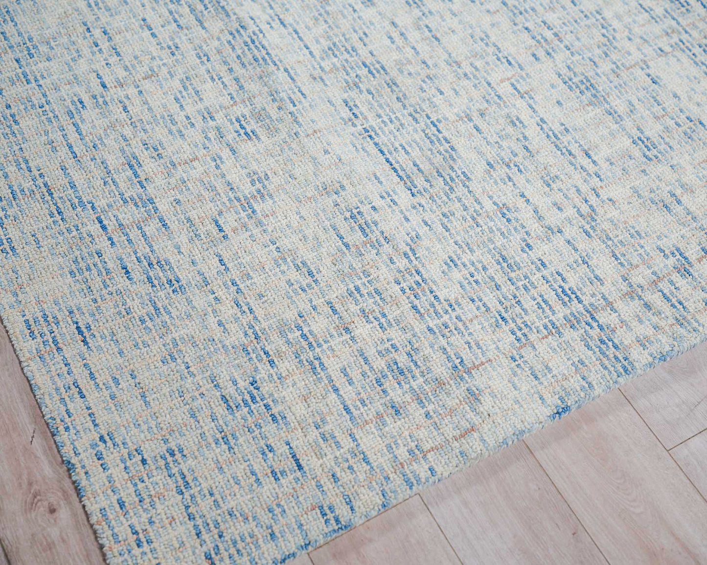 Cream and light blue woven rug with irregular blue lines and textured weave on a light wooden floor.