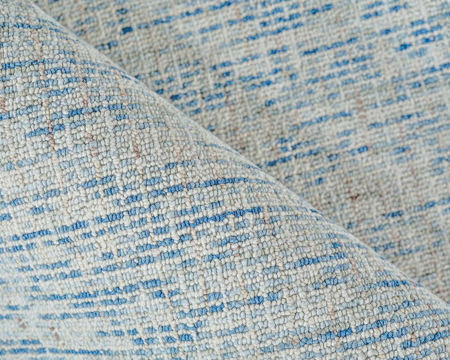 Close-up of light gray hand-tufted rug with blue specks and textured boucle yarn.