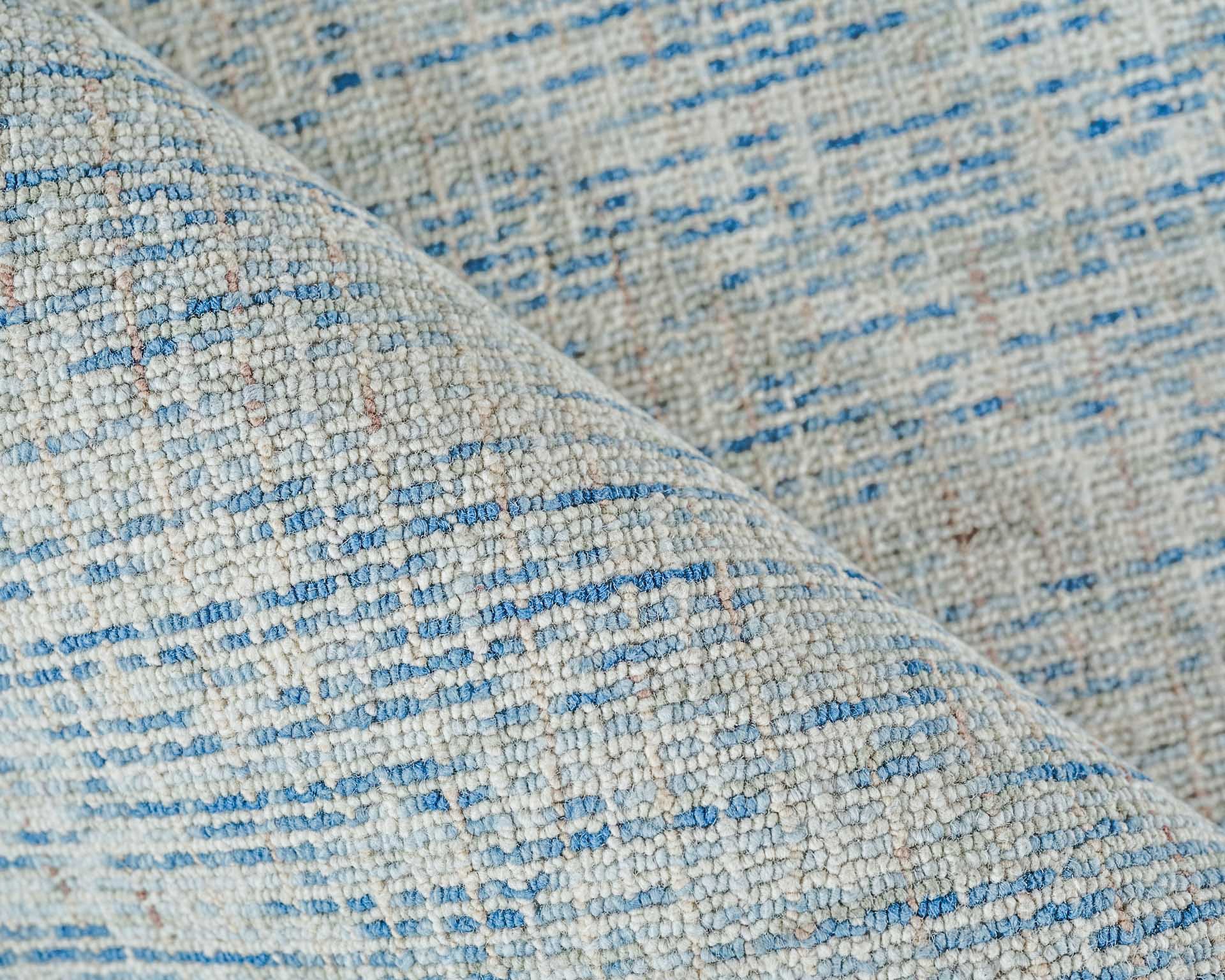 Close-up of light gray hand-tufted rug with blue specks and textured boucle yarn.