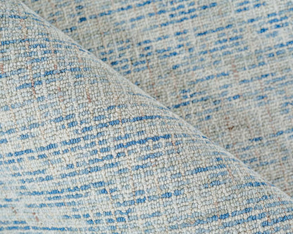 Close-up of light gray hand-tufted rug with blue specks and textured boucle yarn.
