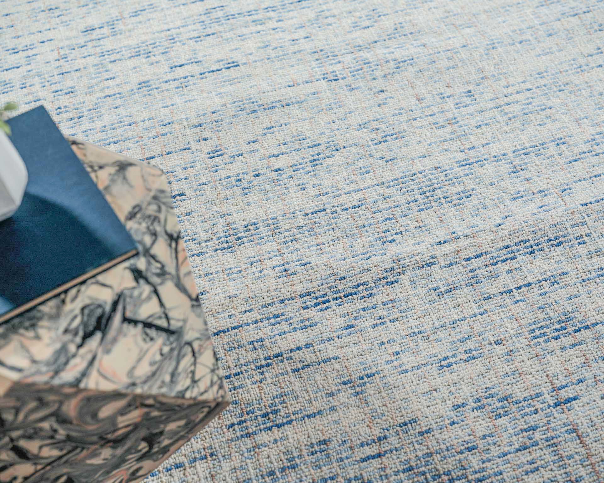 Beige hand-tufted rug with blue streaks; corner features a marbled-pattern box & a dark blue notebook.