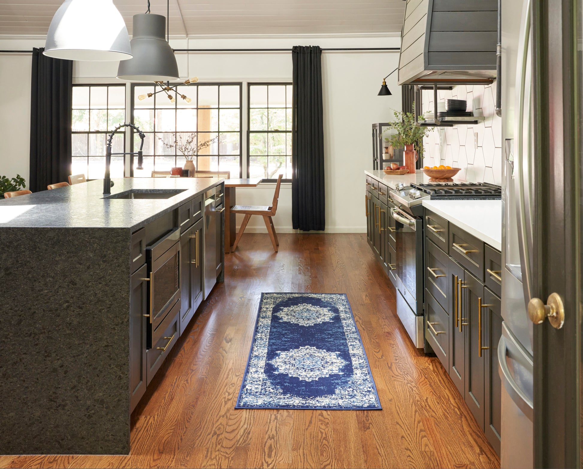 Vintage 8' navy-toned runner rug on hardwood floors in a modern gray kitchen with dark cabinetry, brass pulls, granite island and stainless appliances.