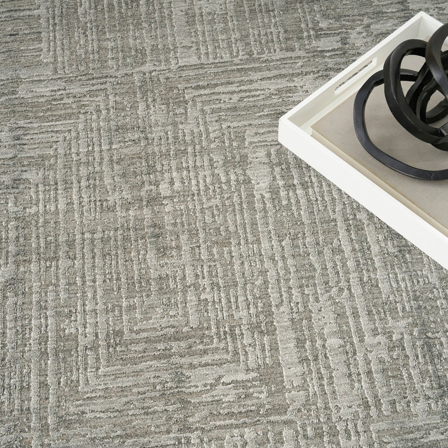 Gray textured carpet with a geometric linear pattern; white tray in the corner holds black circular metal rings.