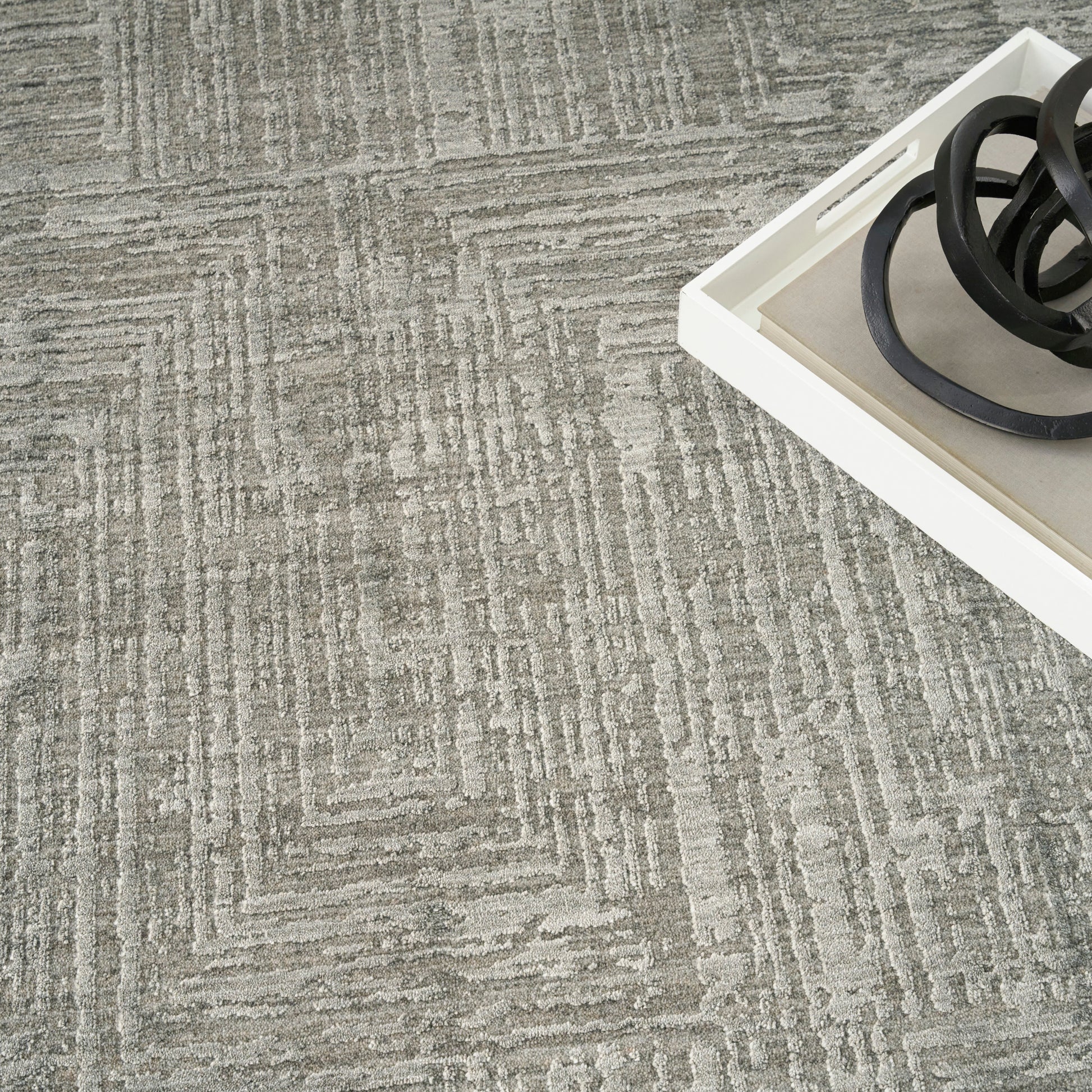 Gray textured carpet with a geometric linear pattern; white tray in the corner holds black circular metal rings.