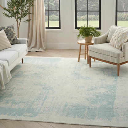 Bright living room with pale blue/cream abstract rug, white fabric sofa & armchair, light wood furniture, plant & round side table.