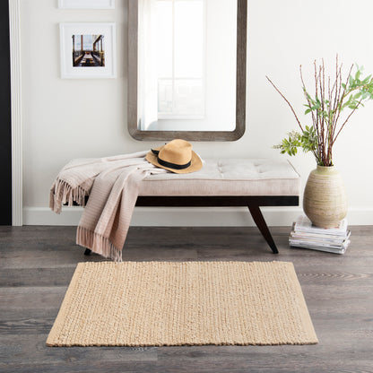 Beige tufted bench with dark legs, tan throw, straw hat, round mirror, photos, vase of branches, magazines, and a jute rug.