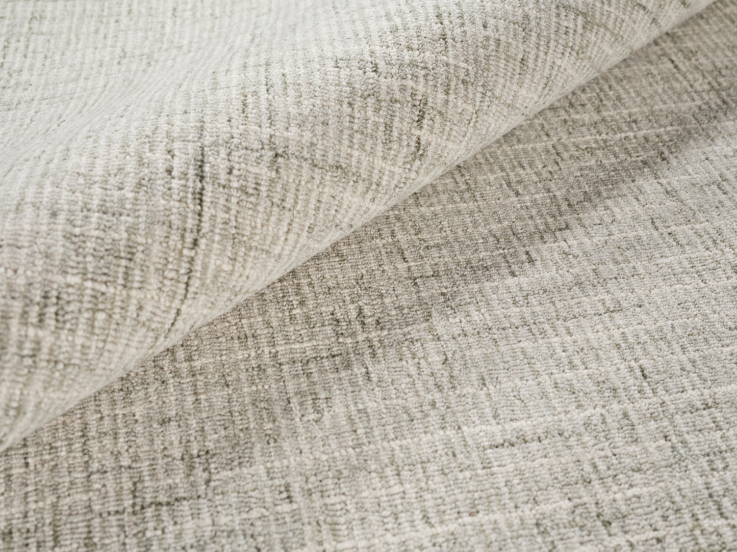 Beige-gray textured woven rug close-up with folded edge; hand-tufted.