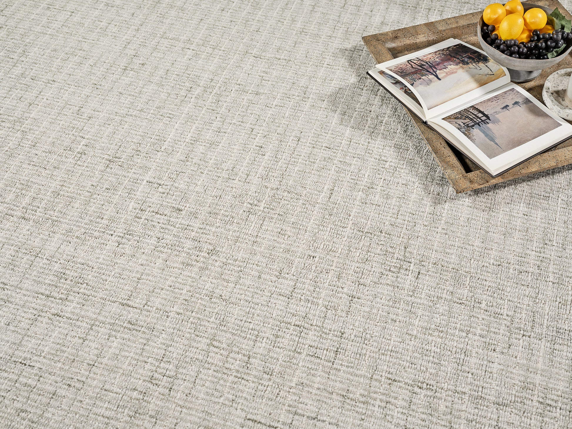 Beige textured rug with a wooden tray holding an open photo book and a bowl of lemons and blueberries.