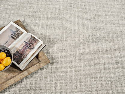 Beige textured rug with a rustic wooden tray holding an open travel book and a bowl of lemons and grapes.