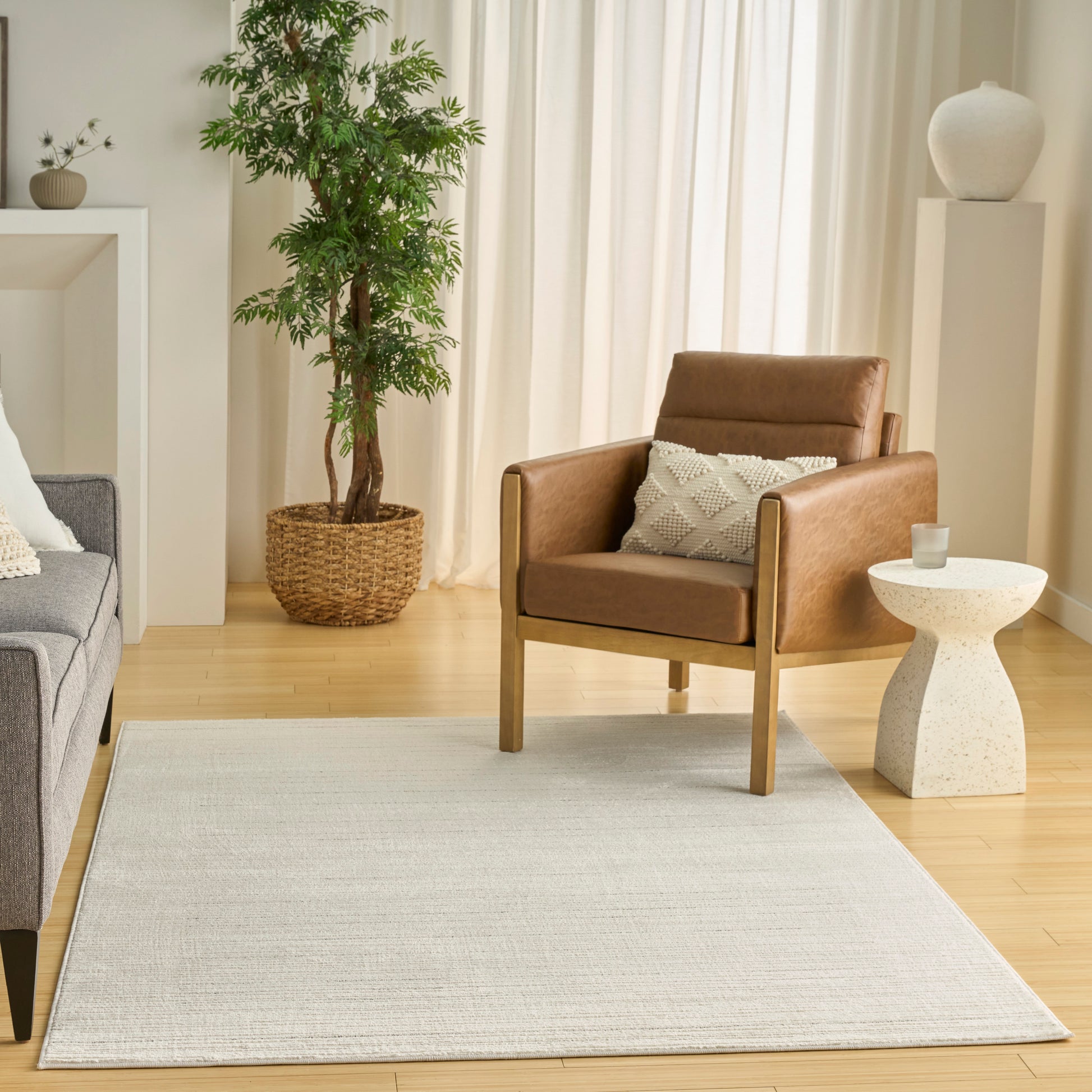 Light beige rug in a modern living room featuring a brown leather chair with wood legs, a gray sofa, and greenery.