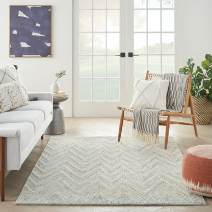 Modern living room featuring a light sofa, wooden accent chair, chevron rug, abstract blue wall art, and plants.