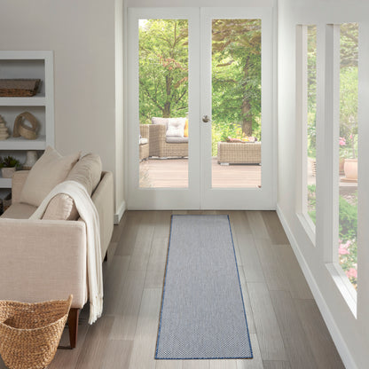 Blue-gray woven runner rug on light wood floor in a bright beige living room with glass doors to a garden patio.