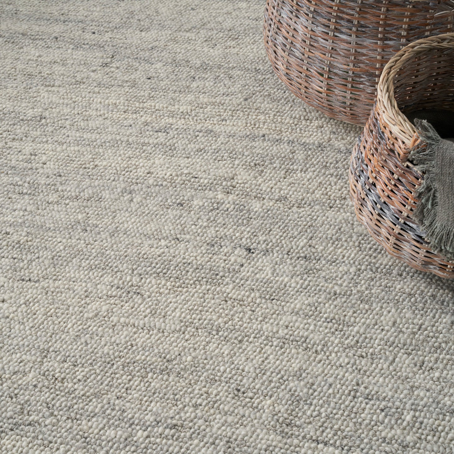 Neutral beige-gray textured woven rug with looped pile; two wicker baskets in the corner.