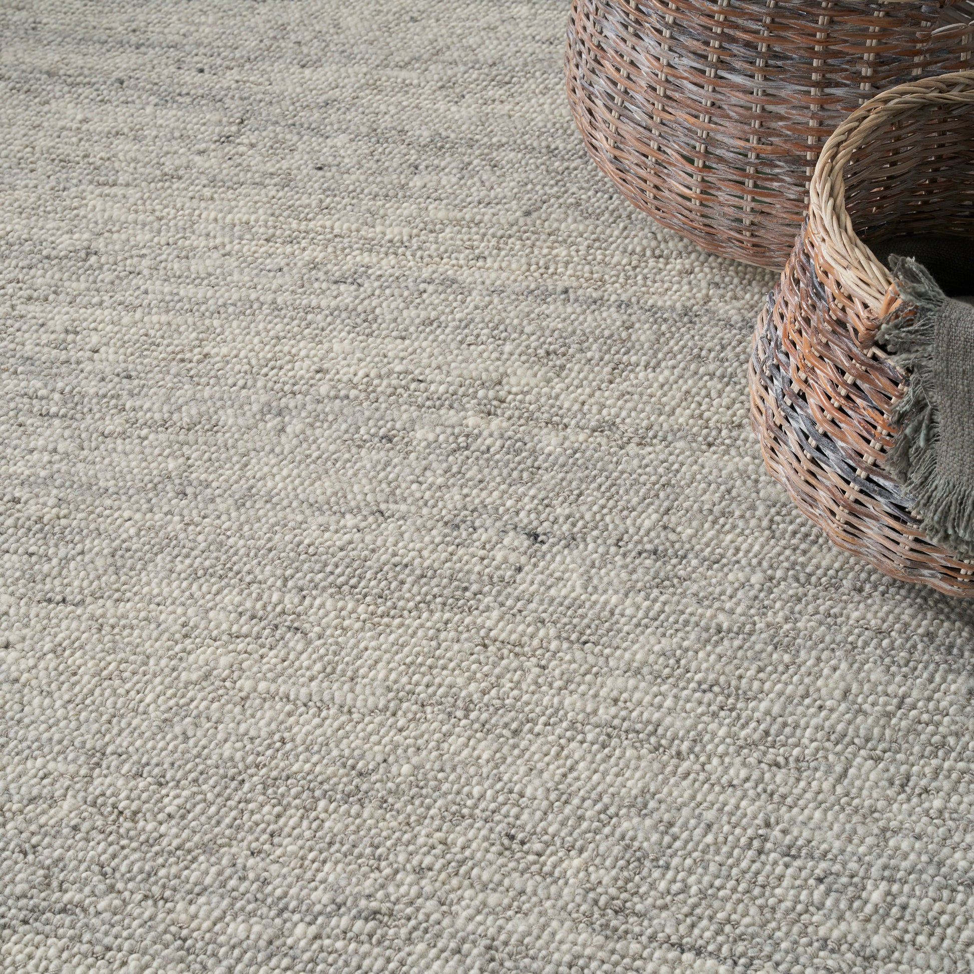 Neutral beige-gray textured woven rug with looped pile; two wicker baskets in the corner.