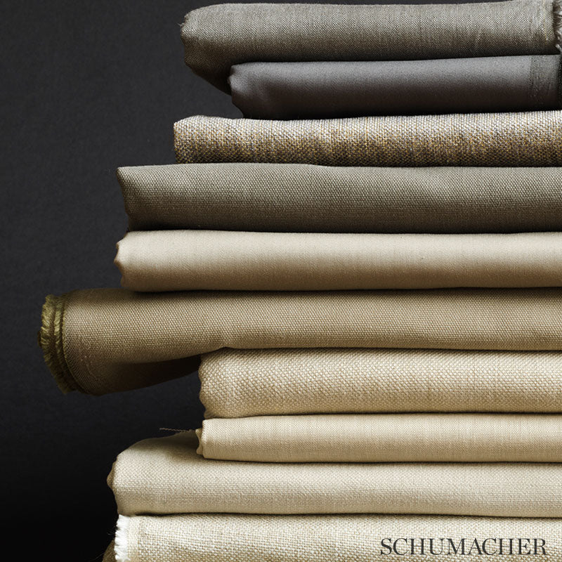 Stack of neutral chenille fabrics in greige tones (beige, taupe, cream), folded with varied textures against a dark background.