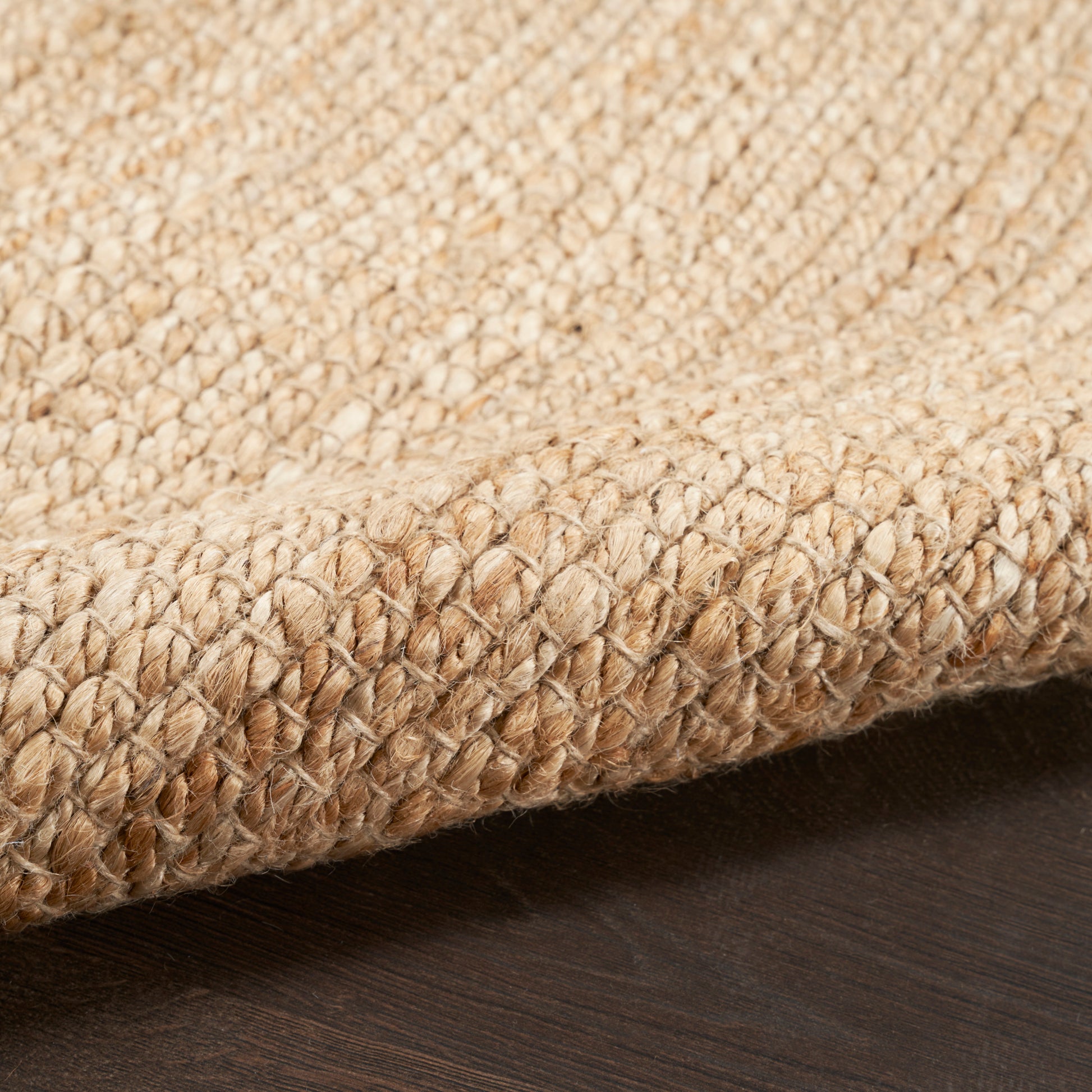 Natural beige jute rug with thick braided texture on dark wood floor.
