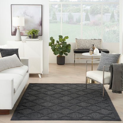 Modern living room with dark gray patterned rug, white sofa, light wood floors, and a glass coffee table by a large window.