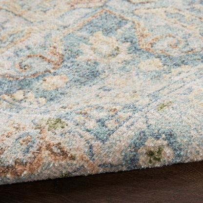 Close-up of a plush blue and beige rug with floral scroll pattern and hints of green on dark wood floor.