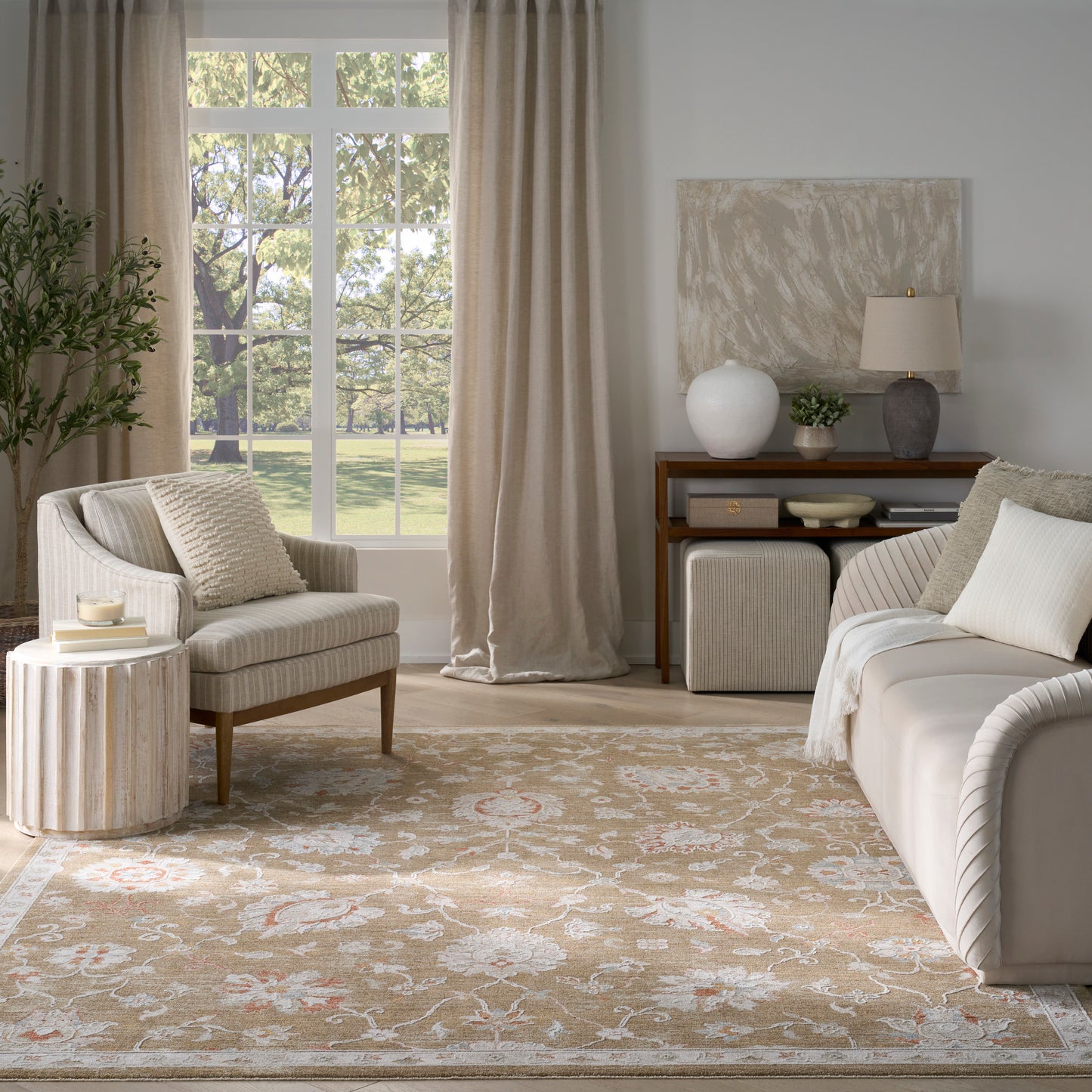 Neutral living room with beige sofa and armchair, light curtains, cream rug, round wood coffee table, console with lamp.