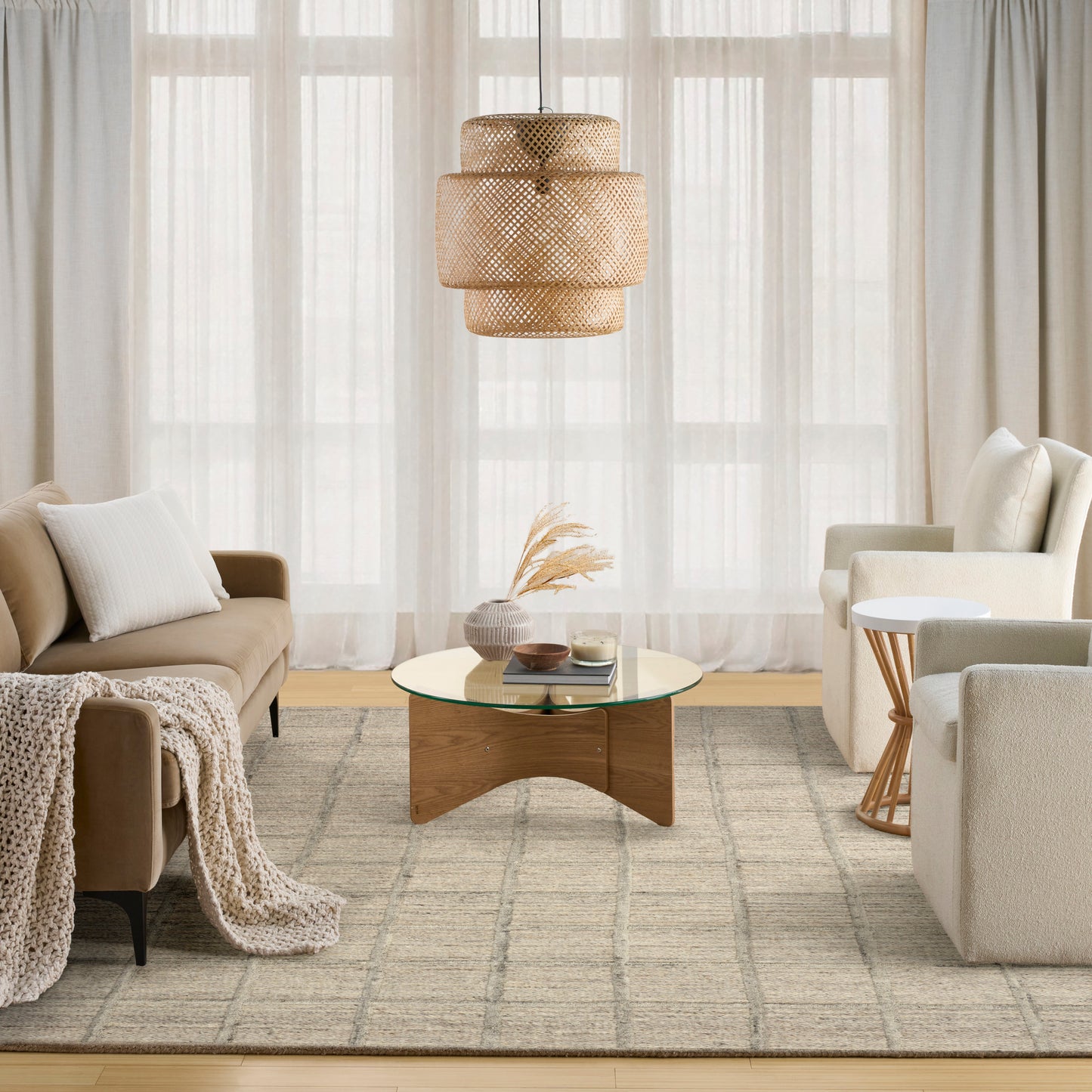 Neutral living room with beige sofa, white cushions, knit throw, round glass coffee table, woven pendant light, beige rug.