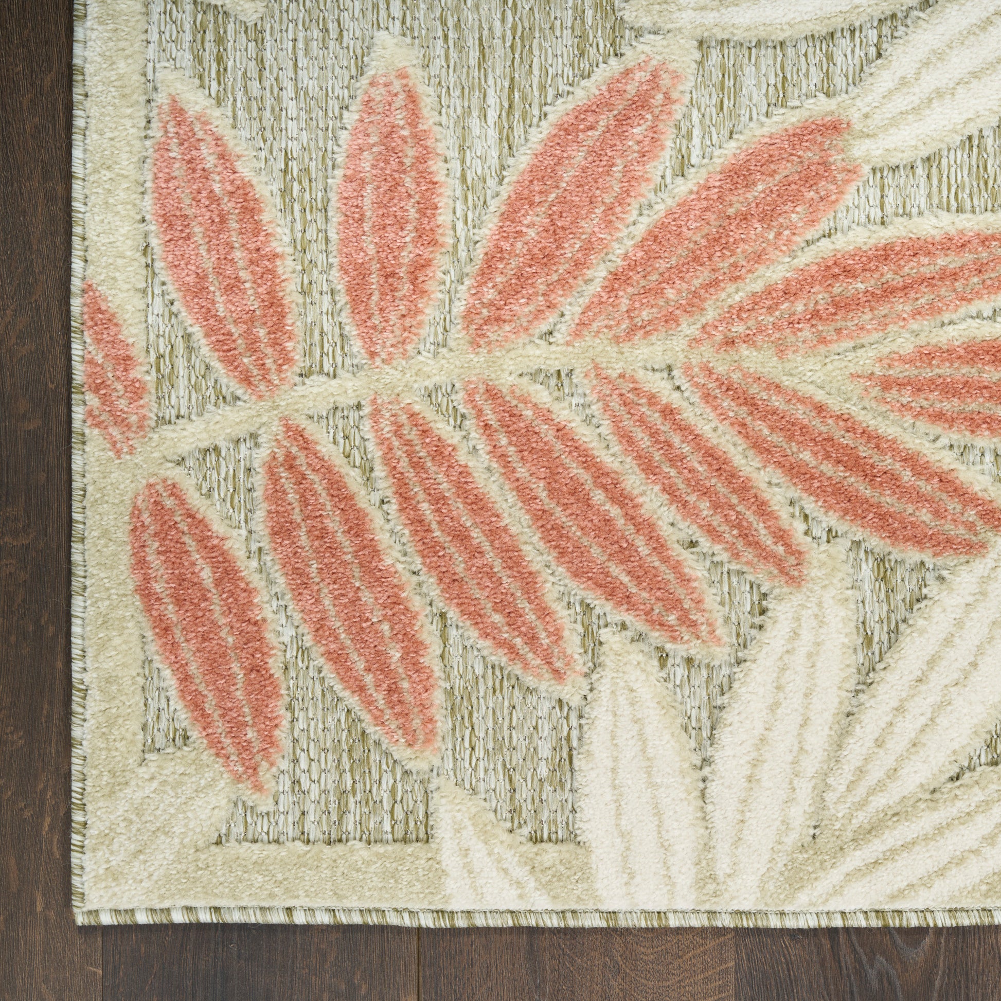Close-up of beige rug with coral-pink palm leaf pattern and textured pile, edge on wood floor.