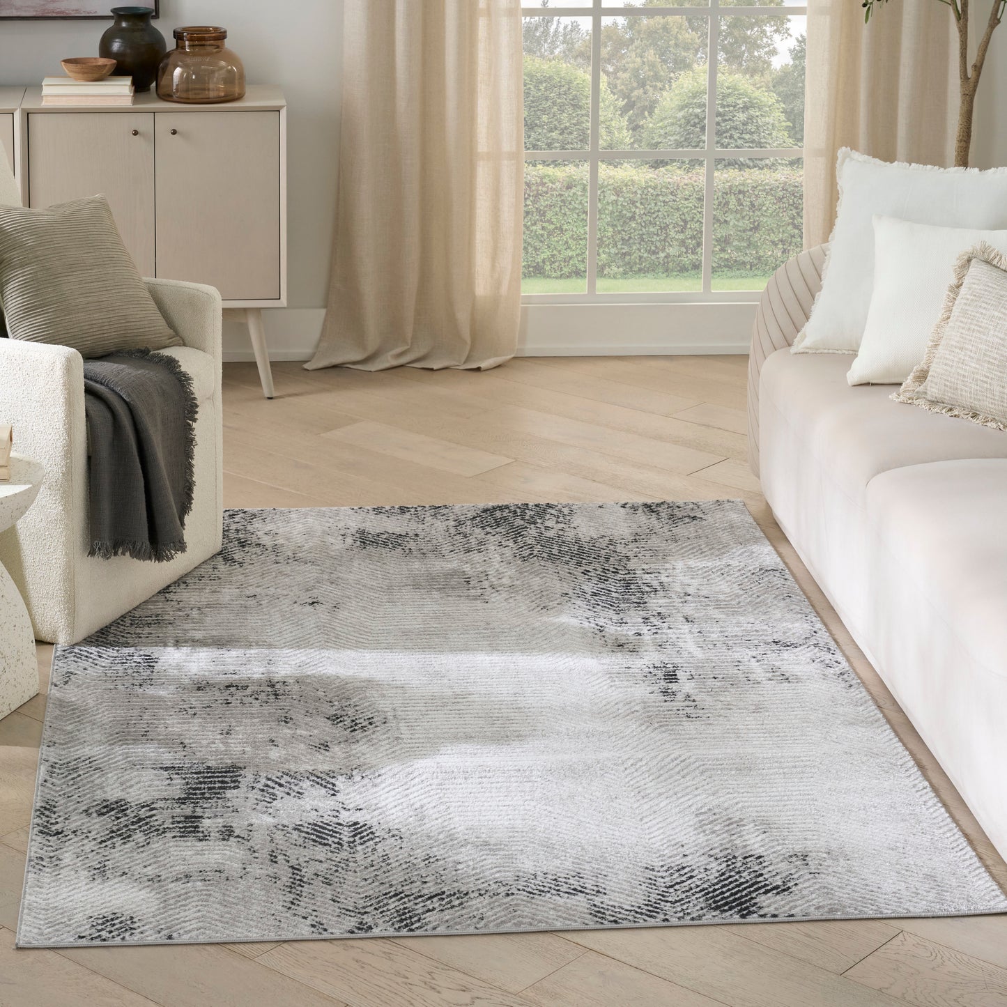 Rectangular gray/black abstract area rug on light wood floor in neutral living room with cream sofa and beige curtains.
