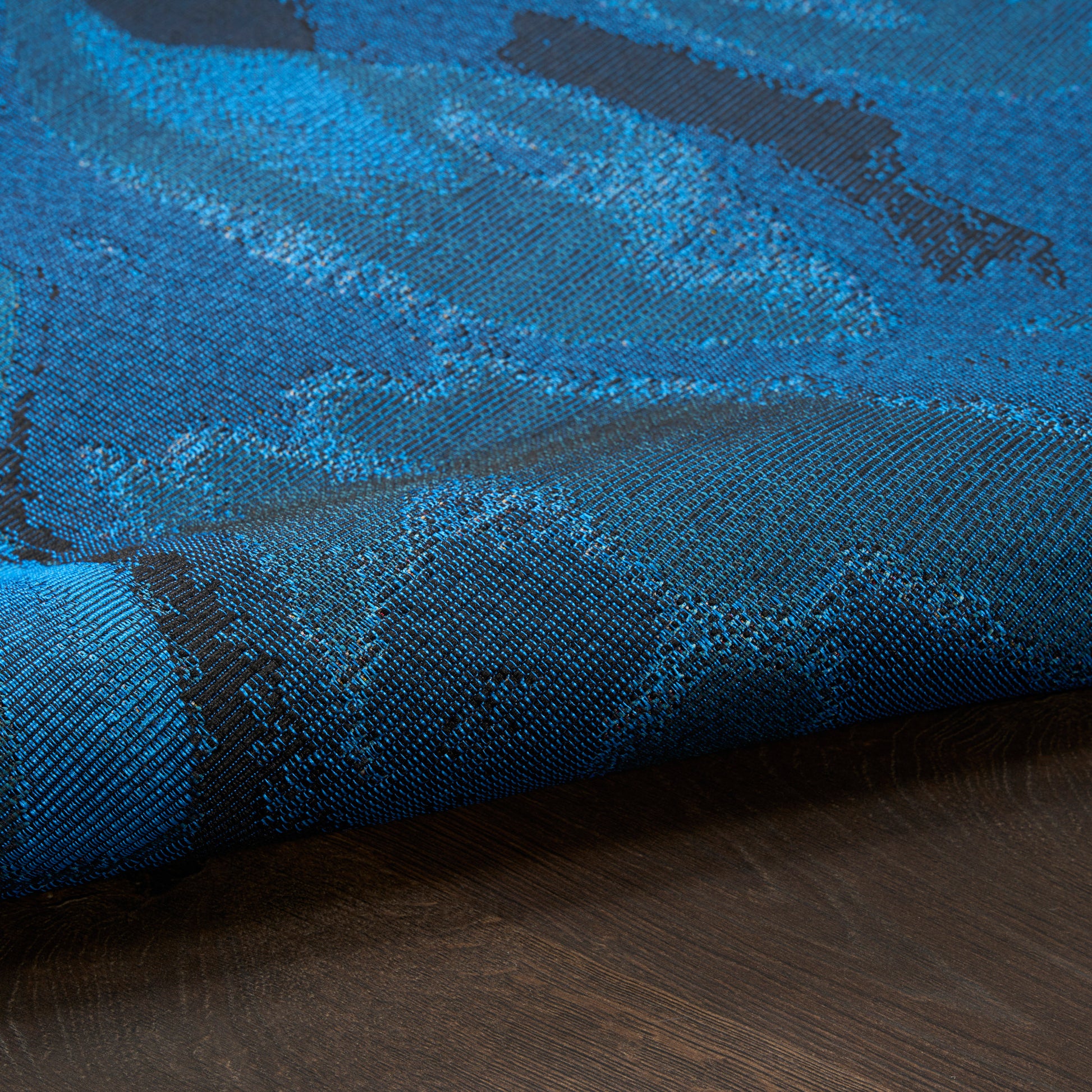 Blue jacquard rug with teal abstract pattern, laid on dark wood floor; modern 5' x 7' rug.