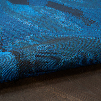 Blue jacquard rug with teal abstract pattern, laid on dark wood floor; modern 5' x 7' rug.