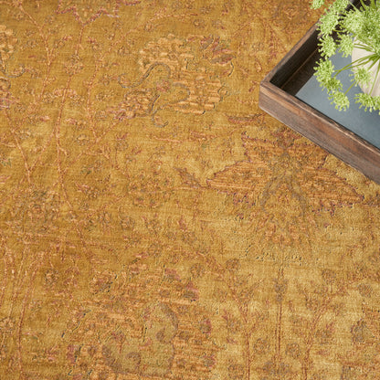 Mustard yellow rug with ornate distressed floral pattern; wooden tray with green plant in the top-right corner