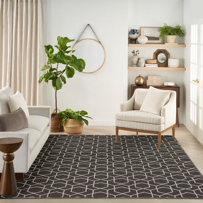 Neutral living room with striped beige armchair, gray sofa, geometric black rug, fiddle-leaf fig in a woven basket, circular wall mirror.