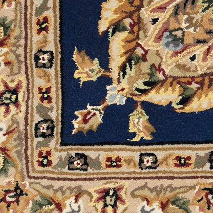 Rectangular oriental rug with deep blue field, ivory-beige border, and multicolor floral vines in gold, red, and green.