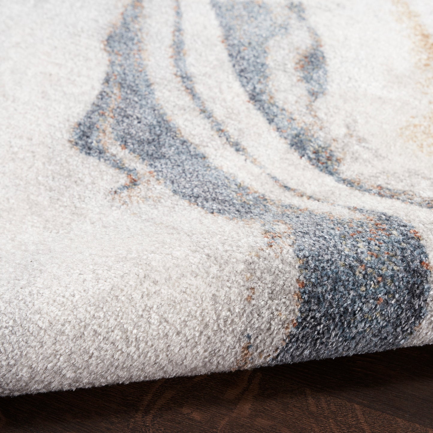 Close-up of a beige textured rug with blue-gray abstract swirl pattern on a dark wood floor.