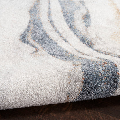 Close-up of a beige textured rug with blue-gray abstract swirl pattern on a dark wood floor.