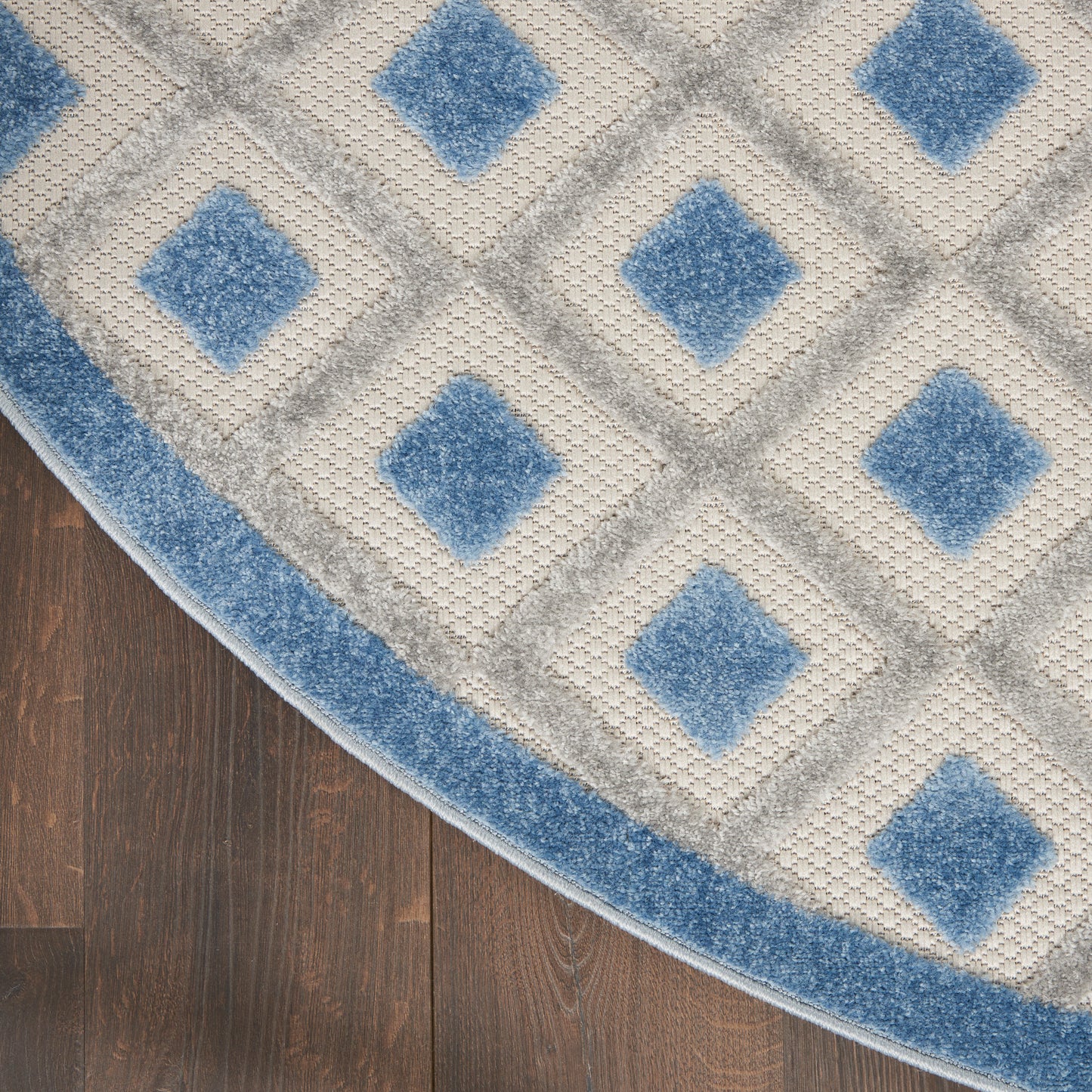 Round area rug with light gray lattice and blue diamond motifs, blue border on dark wood floor.