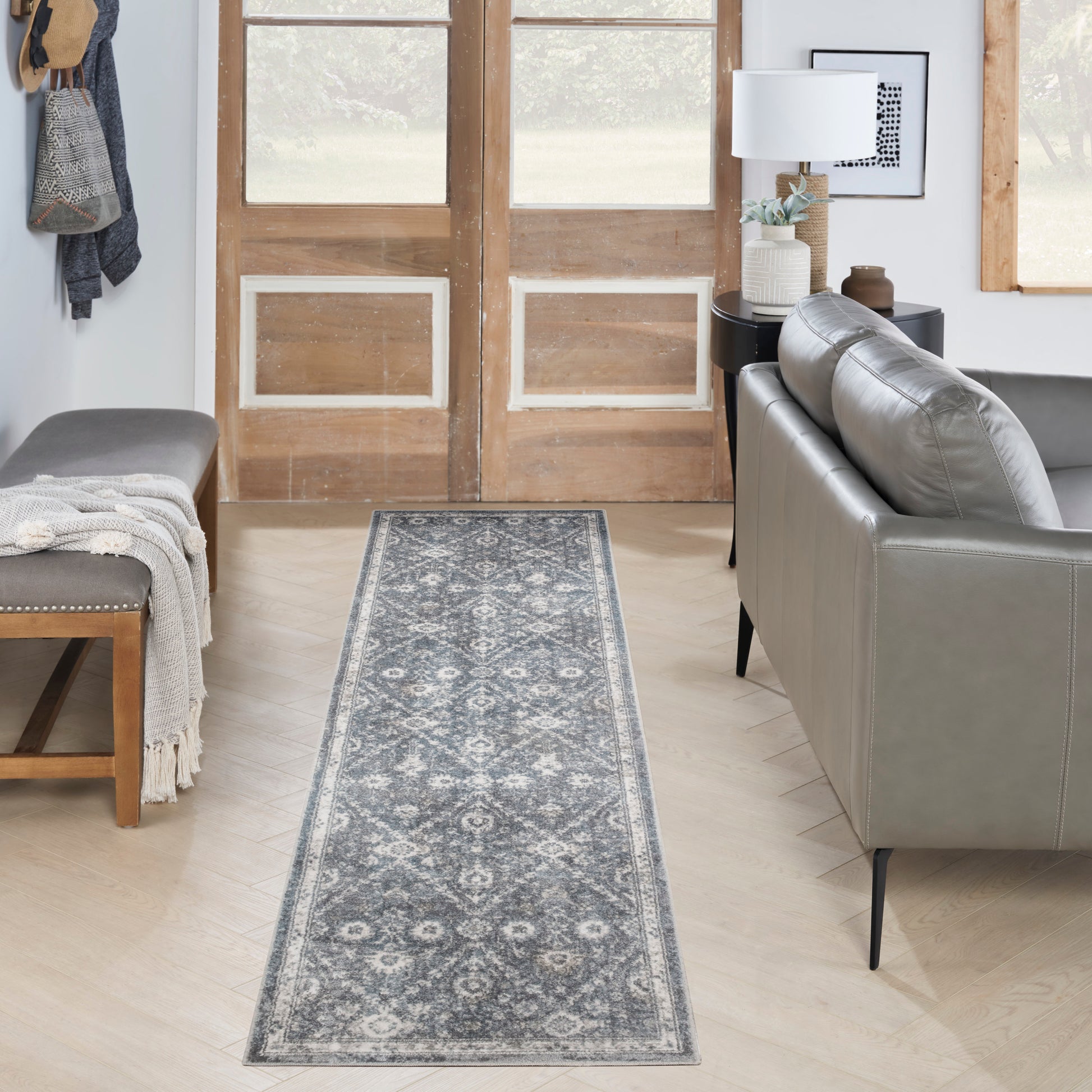Blue-gray patterned 6' runner rug in a light-wood foyer, flanked by a gray sofa and a bench.