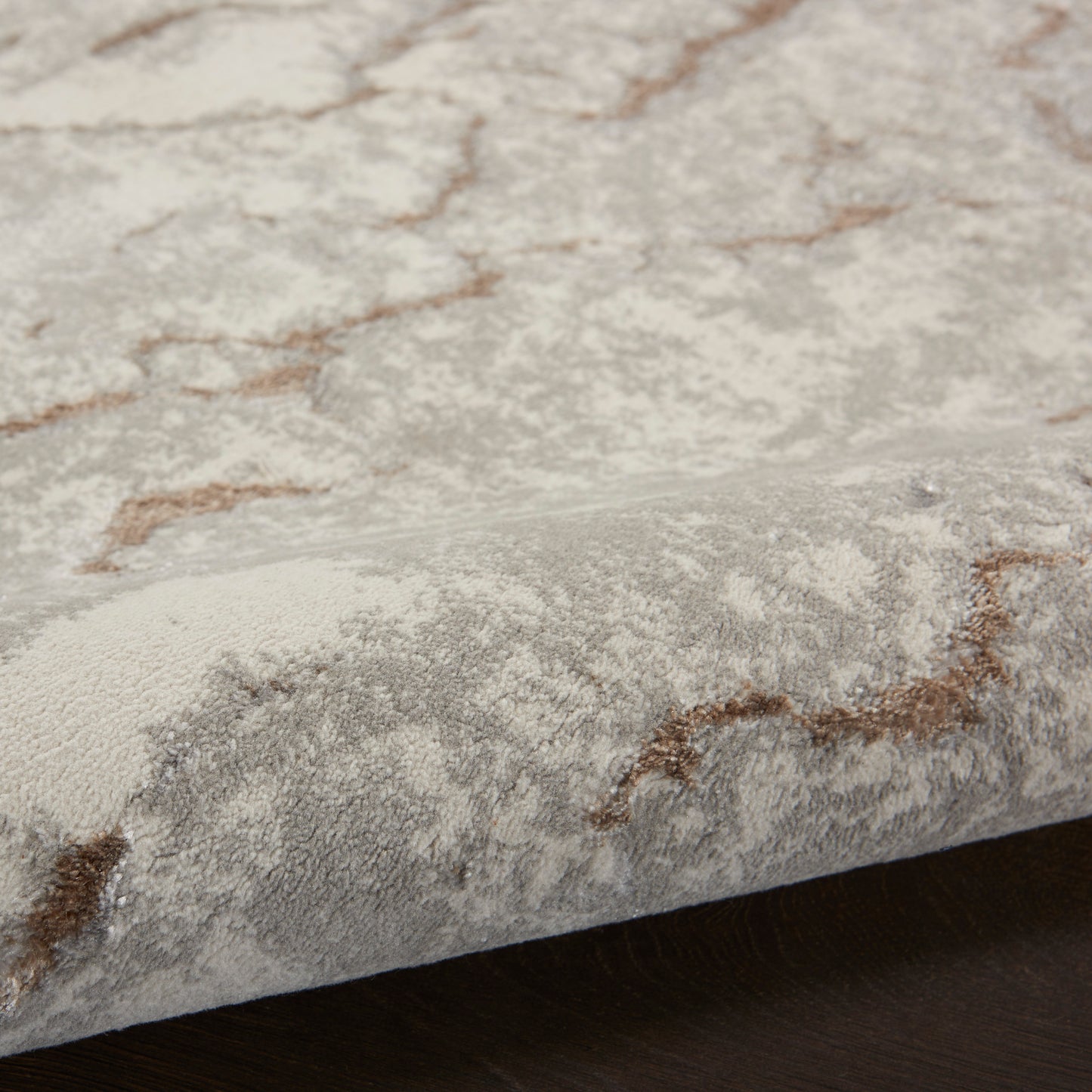 Close-up of a light gray area rug with brown geometric pattern and soft plush pile on dark wood floor.