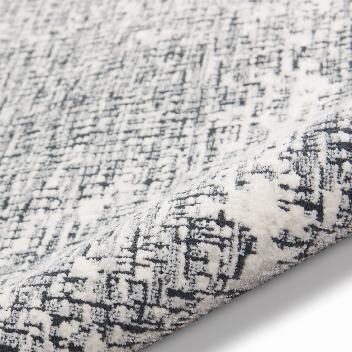 Soft white and charcoal rug with distressed abstract geometric pattern and plush pile.