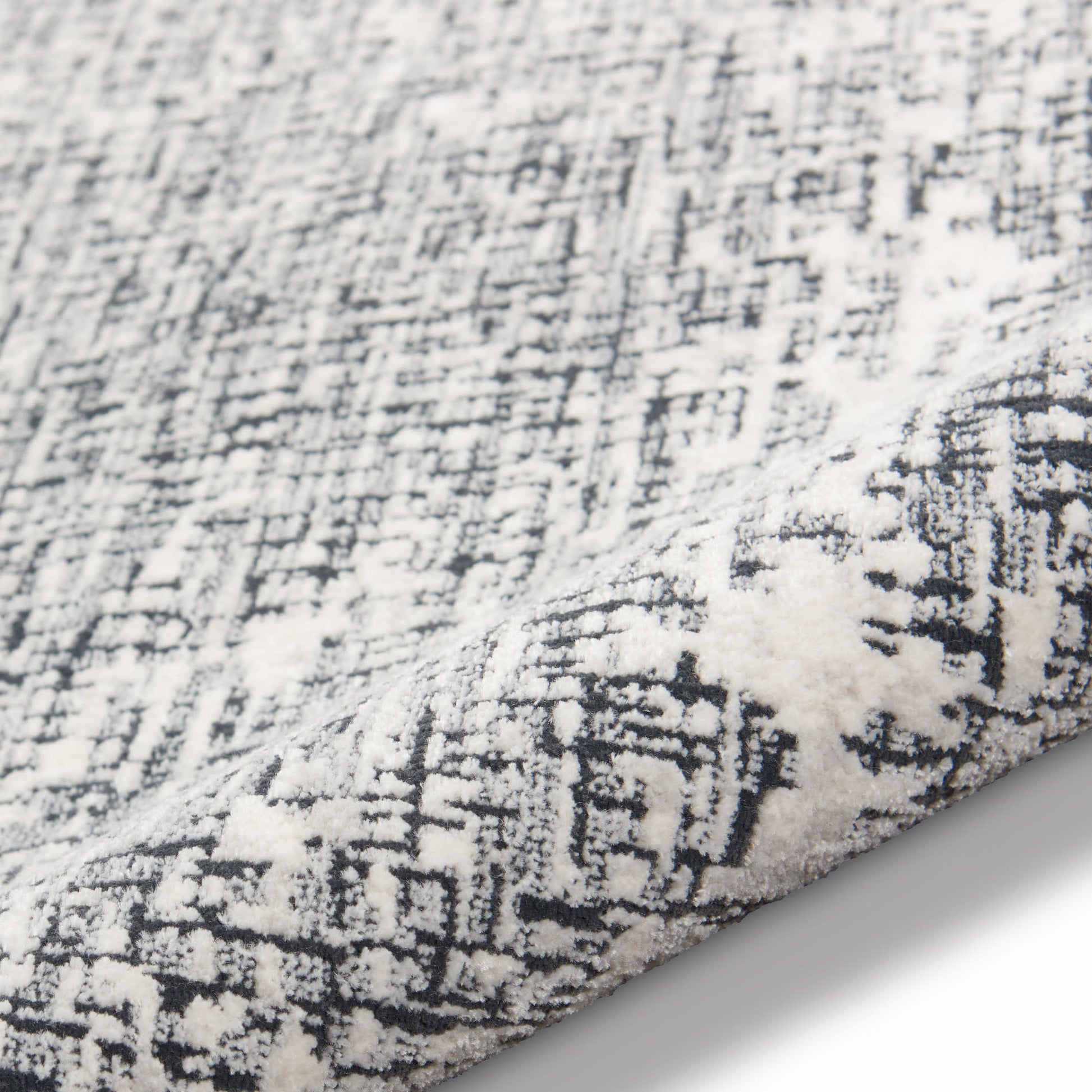 Soft white and charcoal rug with distressed abstract geometric pattern and plush pile.