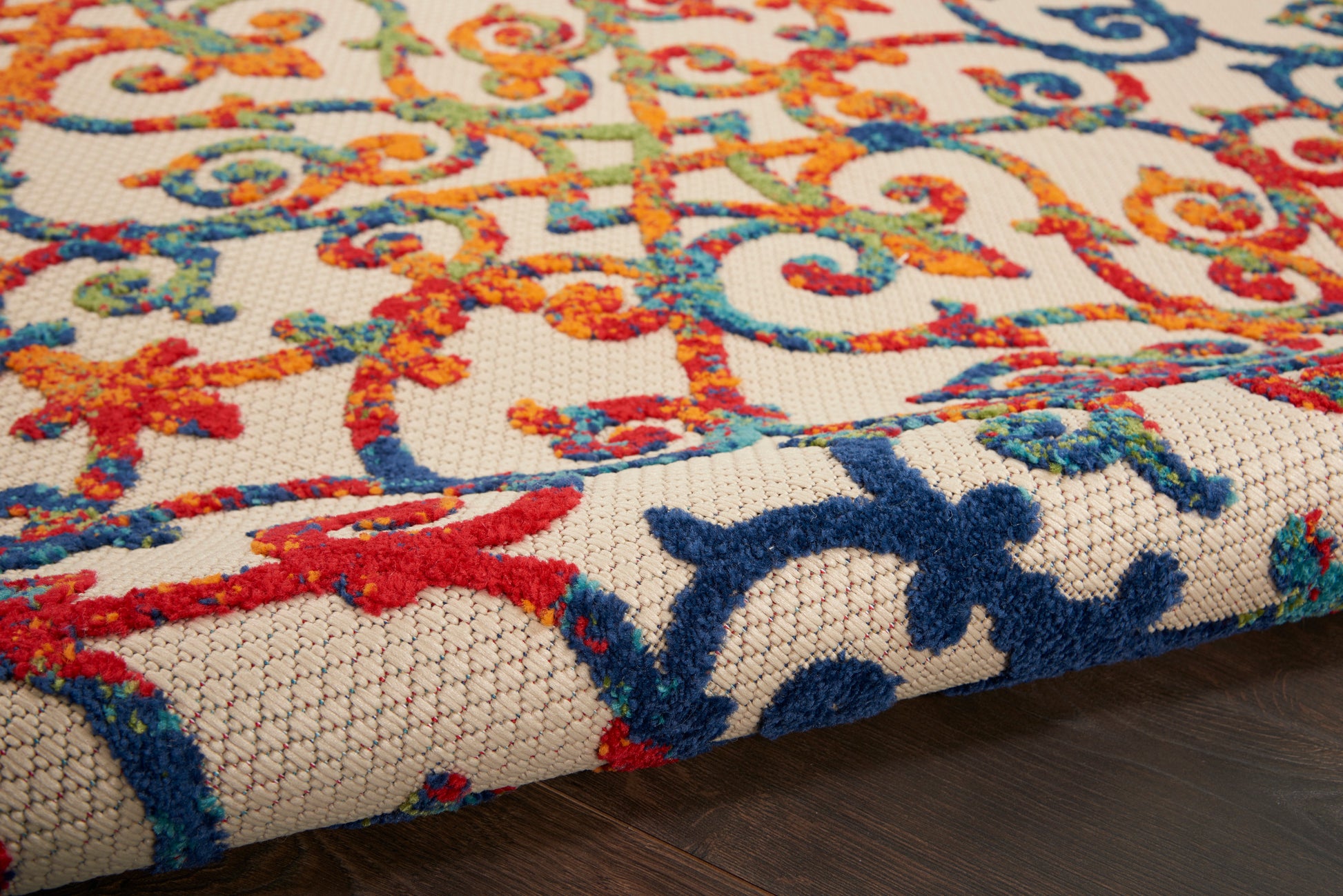 Close-up of colorful oriental-style rug with blue, red, orange scroll motifs on cream woven background; folded edge visible.