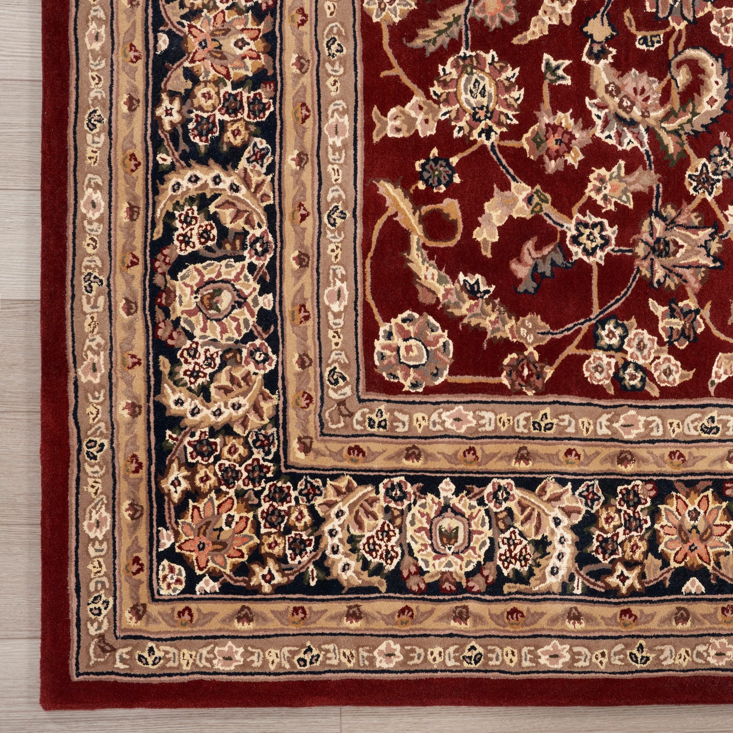 Corner of a Persian-style rug: burgundy field with ivory, navy and gold floral motifs, rich multi-border trim.