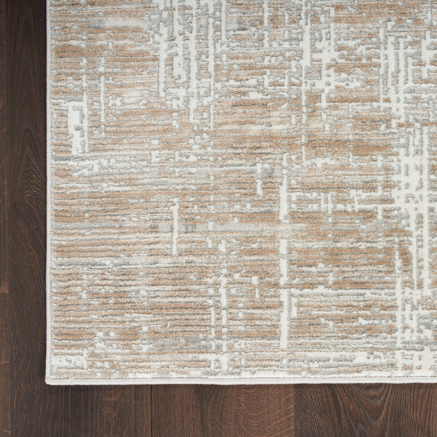 Beige and white geometric patterned area rug with a white border on dark wood floor.