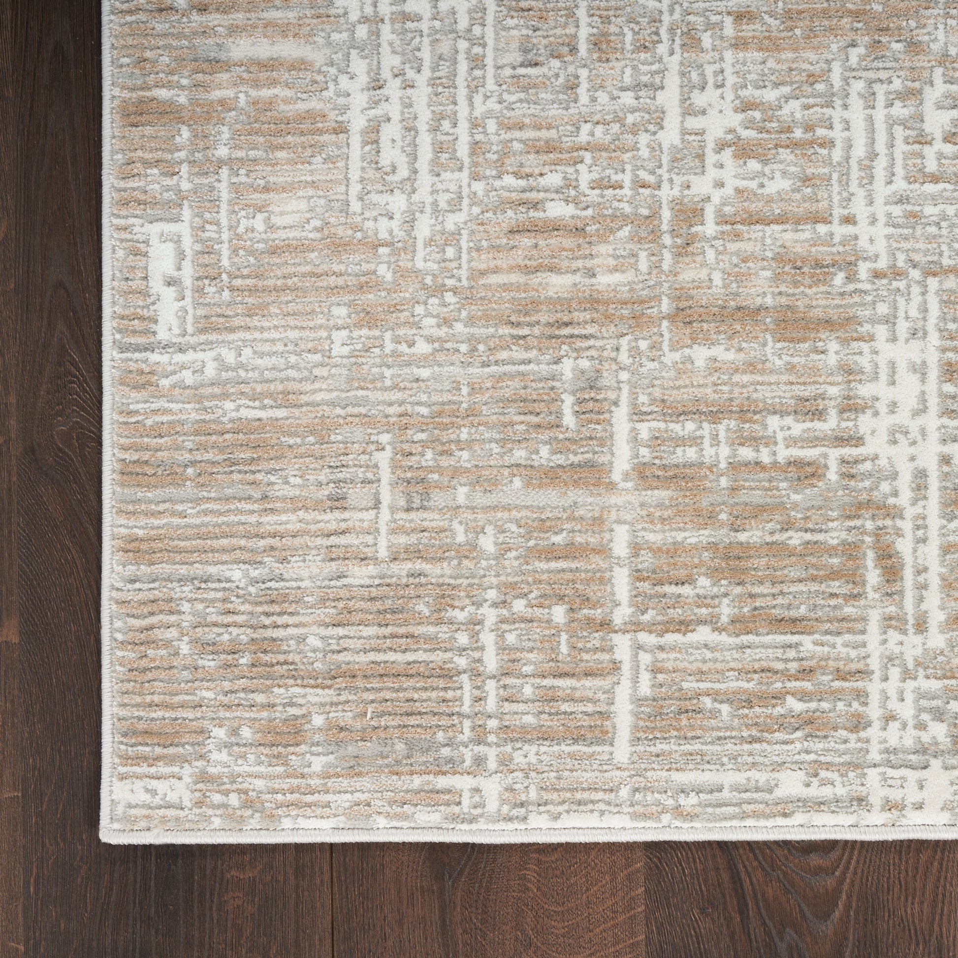 Beige and white geometric patterned area rug with a white border on dark wood floor.