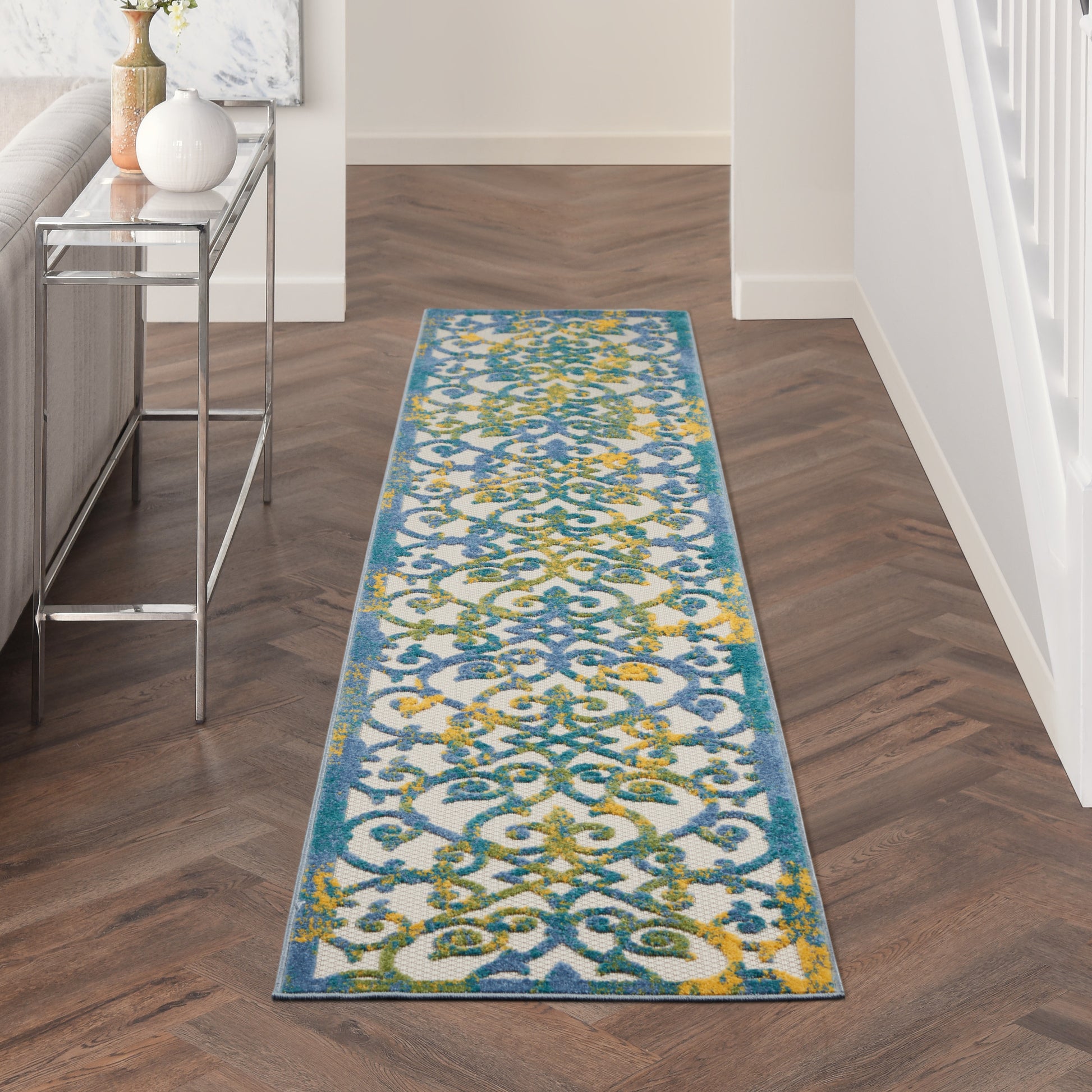 Long runner rug with blue border and ornate blue, green, and yellow damask pattern on white, in a modern hallway.