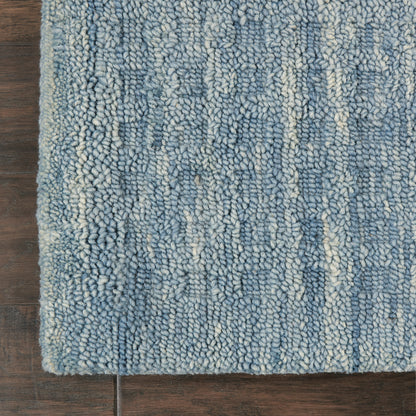 Blue rug with variegated light blue and cream loop pile on dark wooden floor.