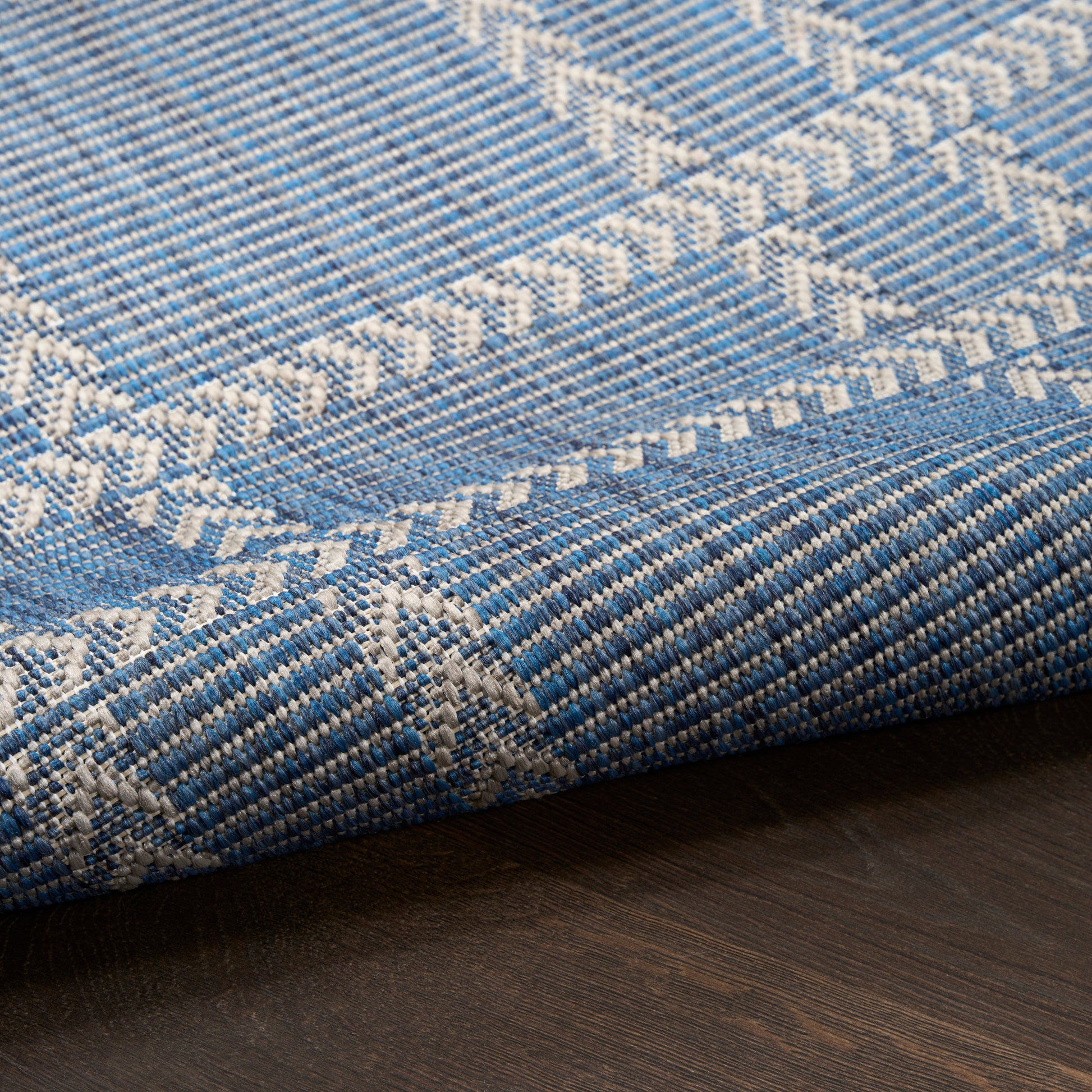 Blue and white woven runner with geometric chevron patterns, folded on dark wood floor.